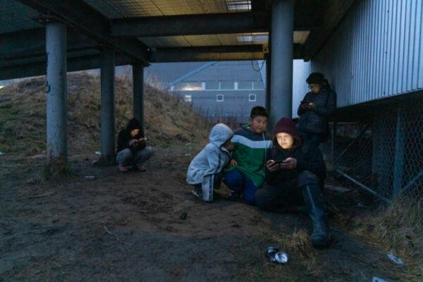 A group of kids sit underneath a deck.